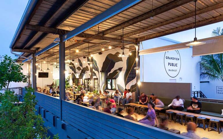 twilight view from outside of patio seating with diners and logo on wall at grandview public market west palm beach