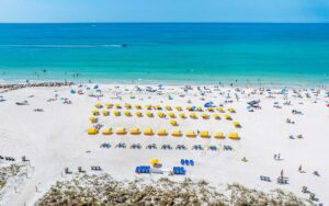 aerial of beach with rows of yellow umbrellas boats people white sand and aqua ocean at st pete beach
