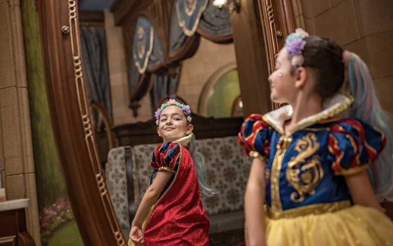 girl in costume smiling at herself in mirror at bibbidi bobbidi boutique at magic kingdom walt disney world resort orlando