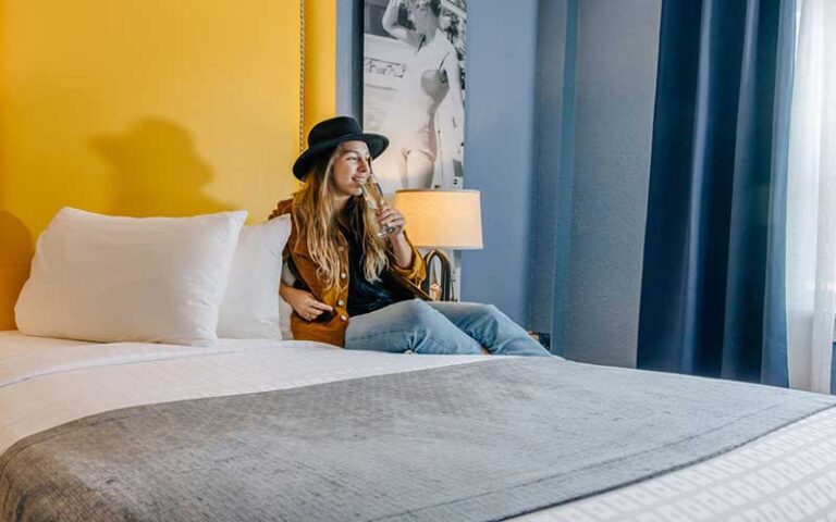 young lady sipping wine sitting on guest bed at hollander hotel st pete