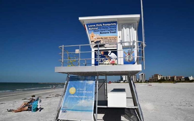 lifeguard building with signs on beach with people in loungers at sand key park clearwater
