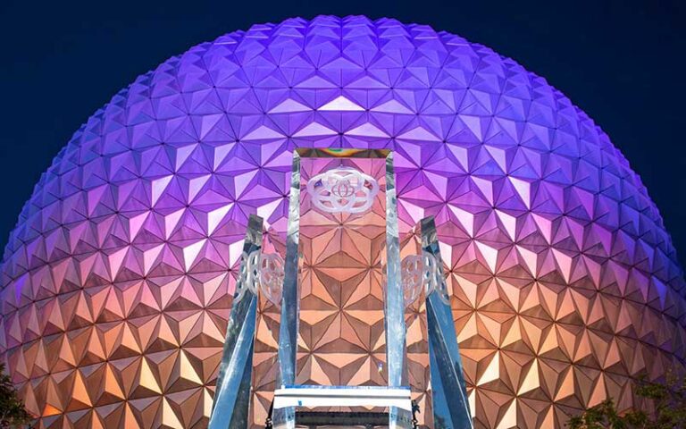 main entrance glass pylons with colorfully lit spaceship earth at night at epcot walt disney world resort orlando