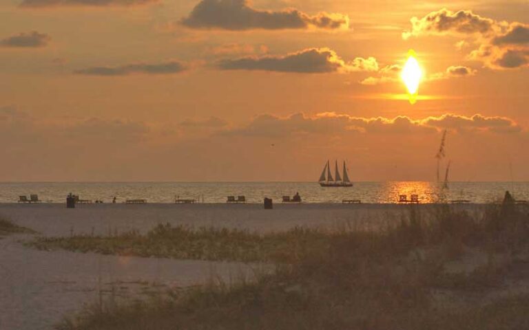 orange sunset over beach and water with sailboat at sand key park clearwater