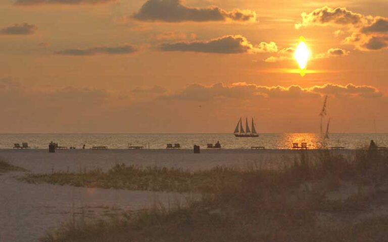 orange sunset over beach and water with sailboat at sand key park clearwater