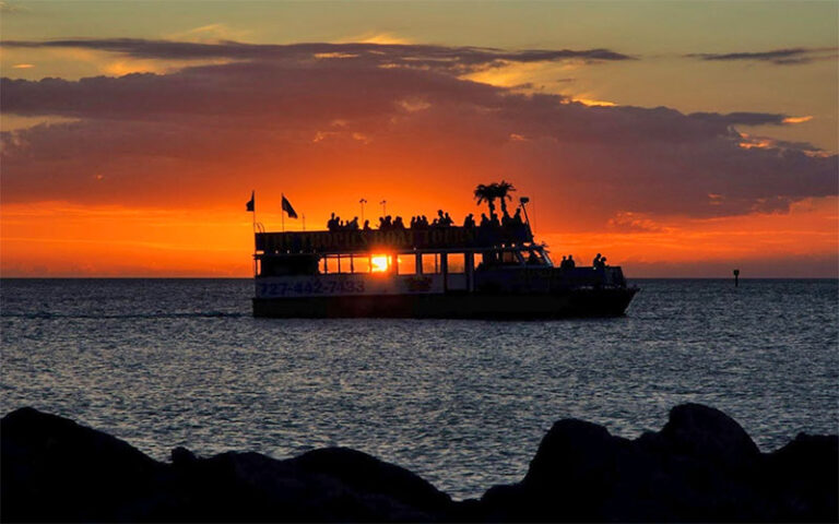 orange sunset seen though silhouette of boat with ocean and rocks at the tropics boat tours clearwater beach