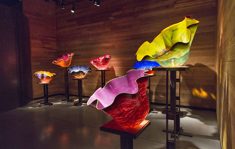 several colorful blown glass bowls on exhibit display in darkened room at chihuly collection morean arts center st pete
