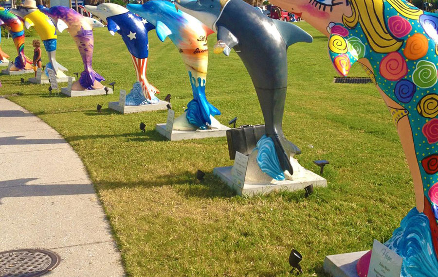 several colorful dolphin statues along curved sidewalk and grass at dolphin trail clearwater