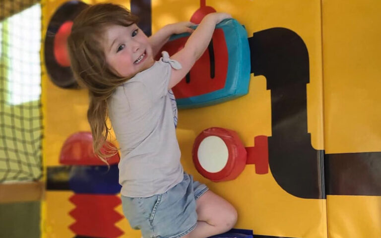 smiling girl climbing padded playground wall at ready set play st augustine