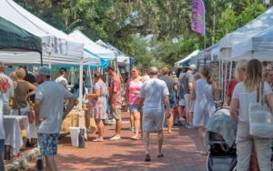 two rows of market stalls with shoppers under trees at safety harbors market on main clearwater