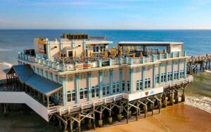 large building on stilted pier along coast with waves and extension at daytona beach main street pier