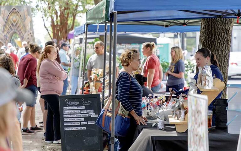 shoppers at market stalls under trees at palafox market pensacola