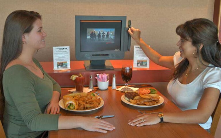 women seated at dining table with entrees using betting kiosk at daytona beach racing card club