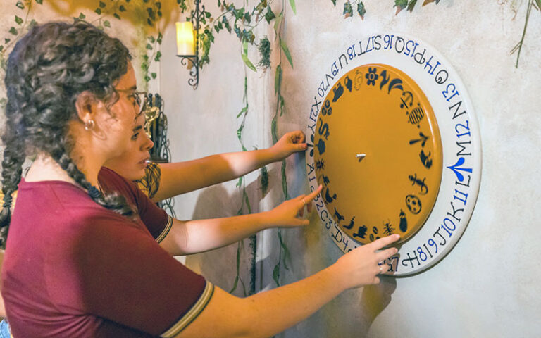 girls turning dial on wall with mysterious characters at amelia island escape rooms