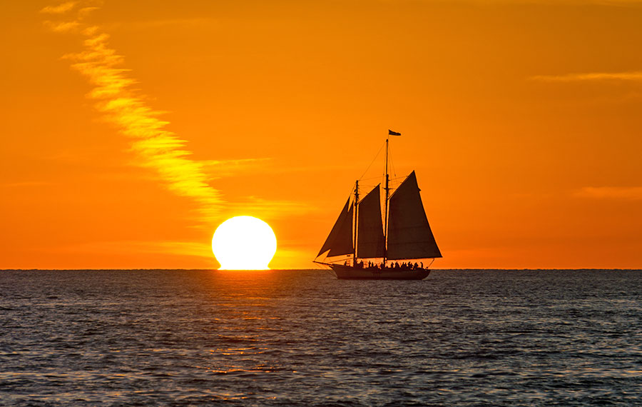 orange sunset over dark water with sailboat silhouette and streaked cloud mallory square key west