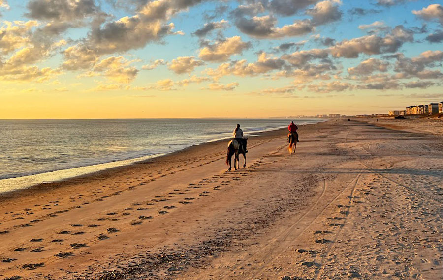 two figures on horses along beach with sunset sky amelia island horseback riding