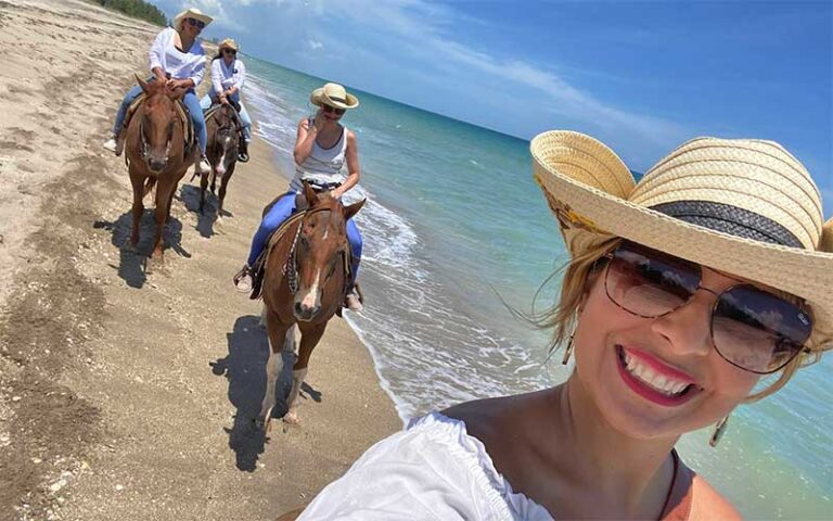 woman taking selfie with horseback women behind on beach at tours on horseback fort pierce