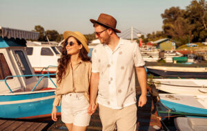 young couple with stylish summer clothes taking a walk on river dock with boats
