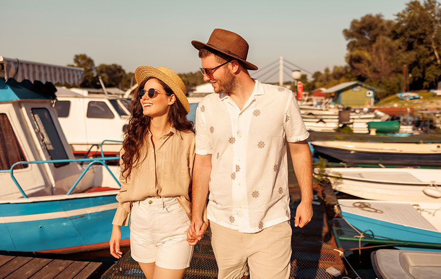 young couple with stylish summer clothes taking a walk on river dock with boats