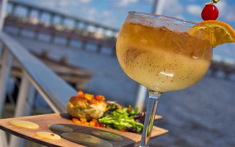 cocktail with garnish and entree on waterfront deck at stuart boathouse