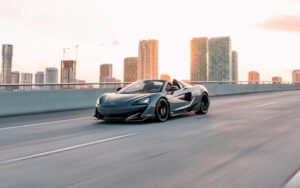 dark gray lotus sports car speeding along highway with high rise skyline at mph club exotic car rental orlando miami