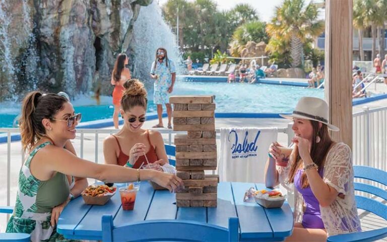 ladies seated at cabana with lively pool and waterfall background at the island resort fort walton beach