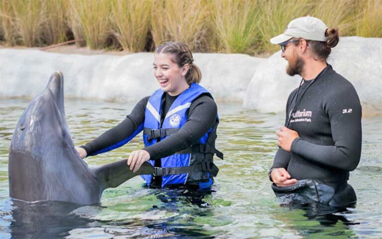 woman holding dolphin by fins with trainer at gulfarium marine adventure park fort walton beach