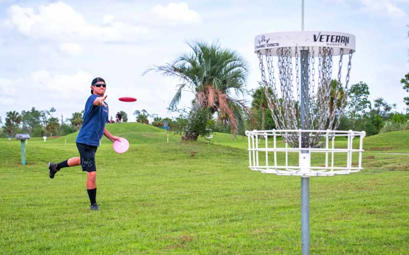 disc golfer throwing to chain stand hole on course