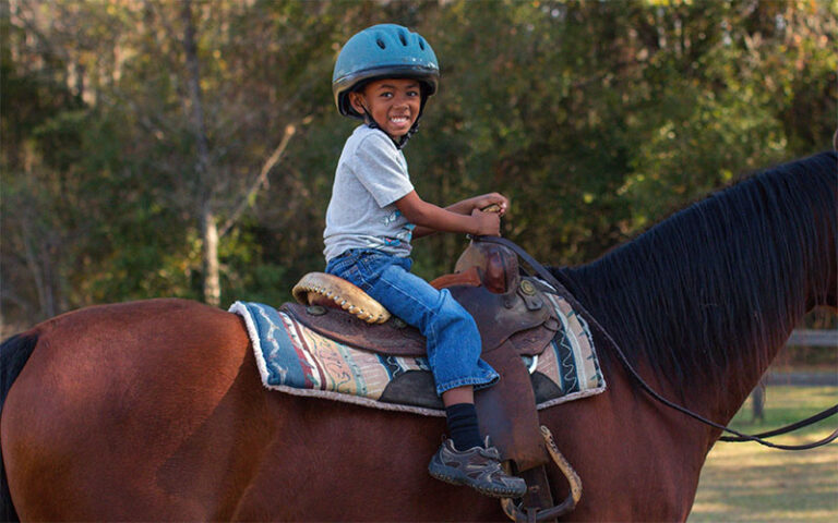smiling young boy with helmet on horseback with helmet at rock springs guest ranch sorrento