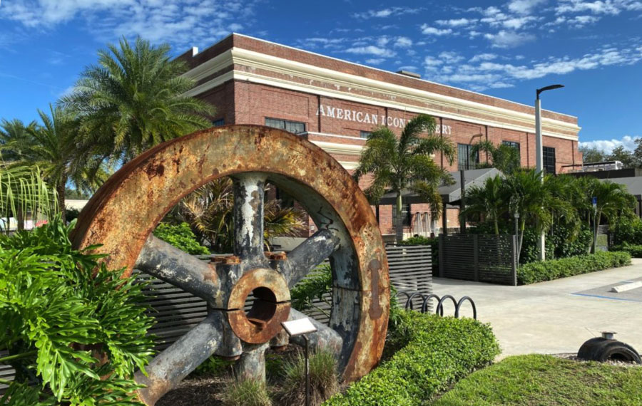 exterior of brick building with large cog wheel displayed in shrubs at american icon brewery vero beach