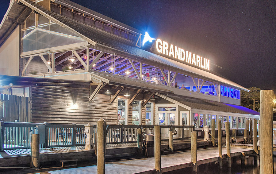 exterior of restaurant on dock at night with lighted sign at grand marlin panama city beach