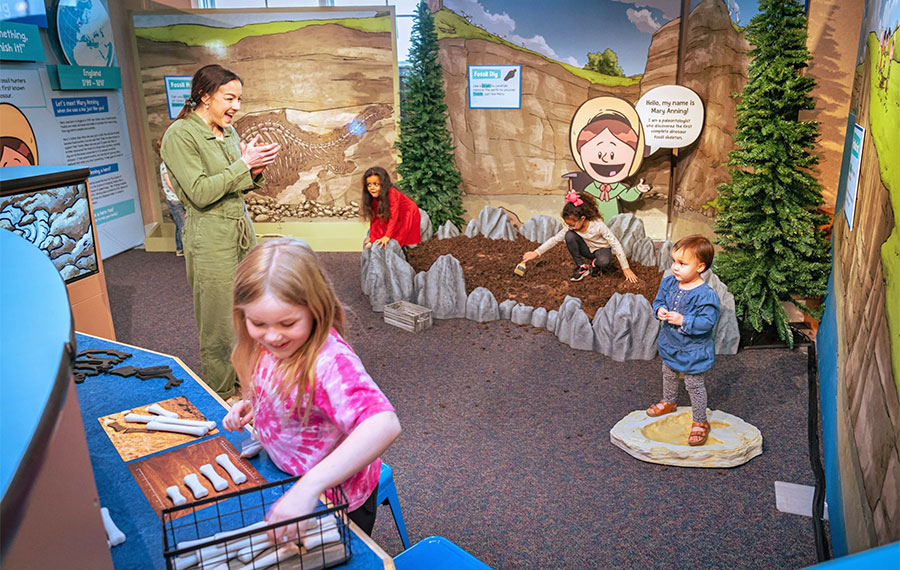 lady and kids interacting in dinosaur dig exhibit at golisano childrens museum naples