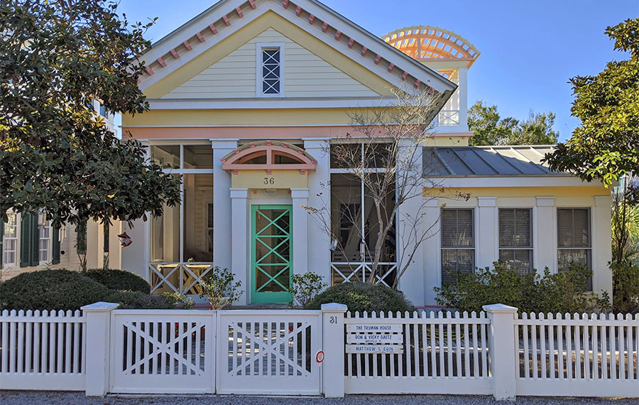 pastel colored house with white fence and sign truman show house at seaside 30a