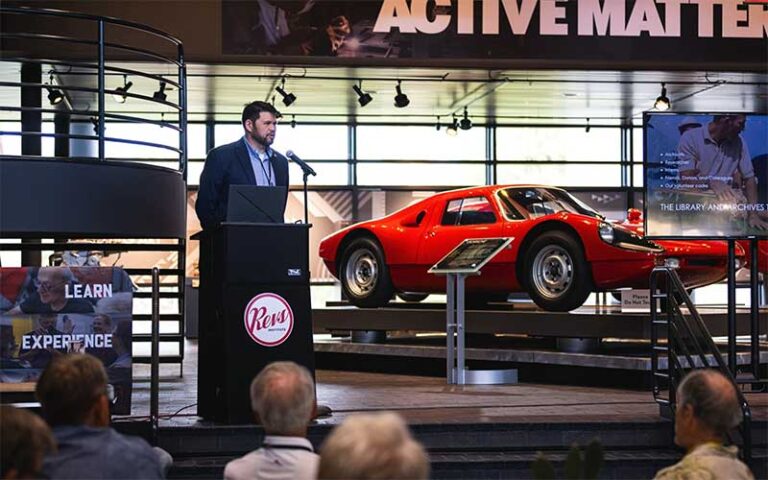 speaker at dais with red ferrari at revs institute naples