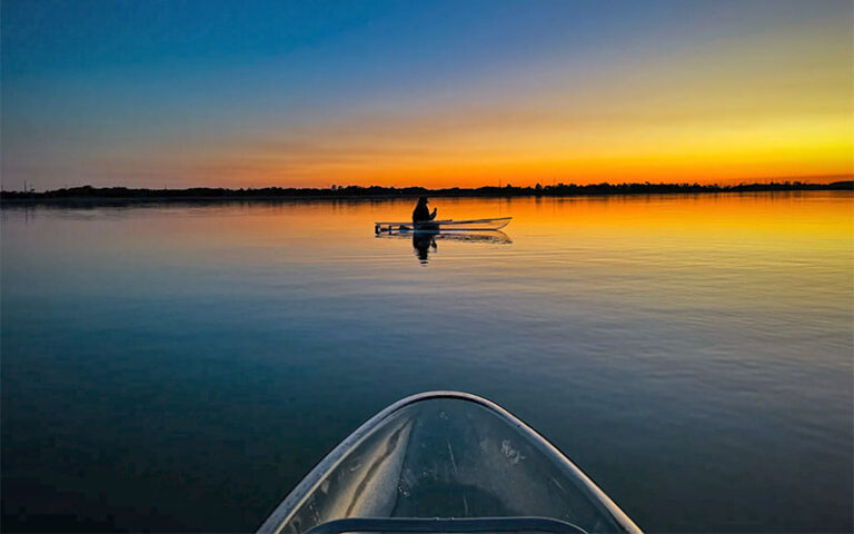 view from kayak of kayaker silhouette on dark water with sunset sky at get up and go kayaking destin