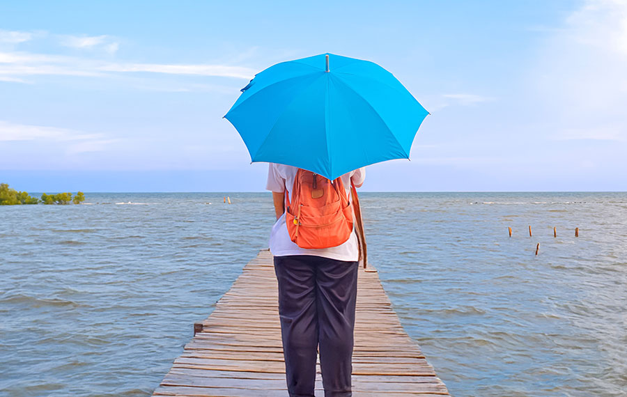 woman with orange backpack holding umbrella on pier overlooking coastal waterway with gray sky