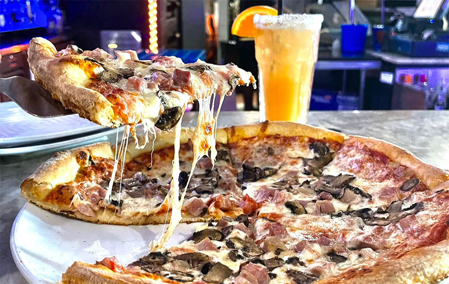 large pizza on countertop with drink and lifted piece at tutto fresco port st lucie