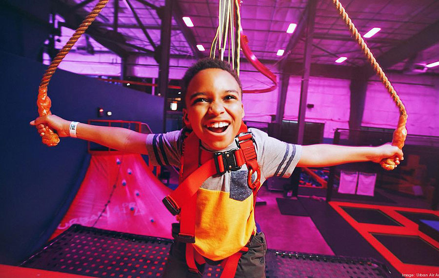 smiling boy riding sky rider zip line indoor at urban air trampoline adventure park