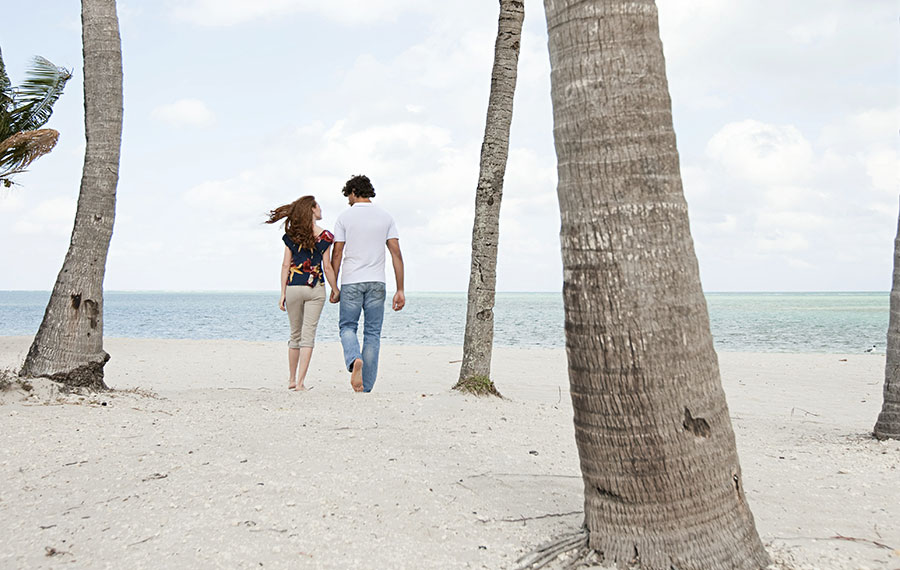 young couple walking hand in hand on beach among palm trees