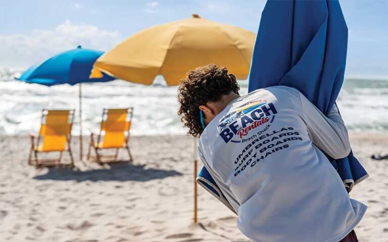 young man putting yellow umbrella in sand at beach shack rentals cocoa beach