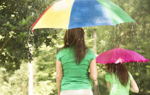 mom and daughter with rainbow umbrellas in park with heavy rain
