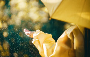 figure with outstretched hand feeling rain from under umbrella