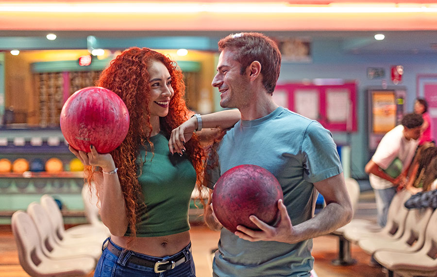 fun couple holding bowling balls and smiling in colorfully lit bowling alley