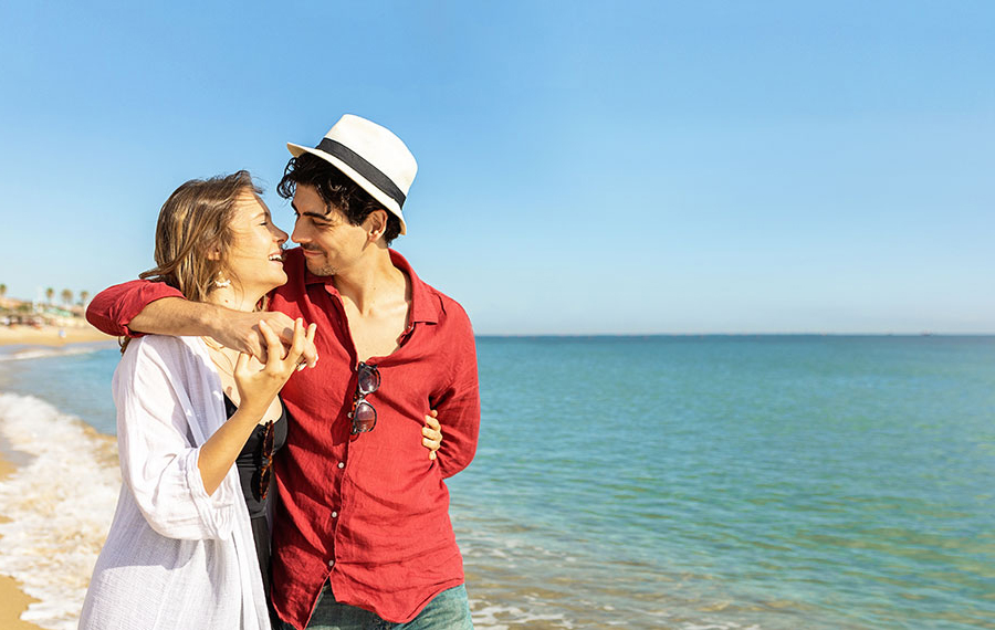 young couple embracing walking together on beach with blue sky inverted