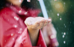 closeup of extended hand feeling rainfall with red raincoat girl