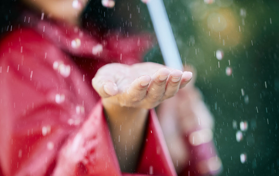 closeup of extended hand feeling rainfall with red raincoat girl