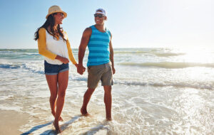 hand in hand young couple walking through surf on beach with bright sun