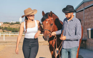 couple wearing western clothes walking with horse at corral