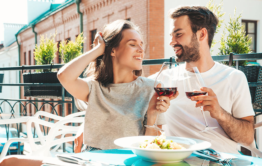 side by side couple toasting wine seated on balcony restaurant downtown