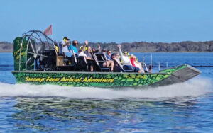 speeding airboat moving across open water with treeline at swamp fever airboat adventures
