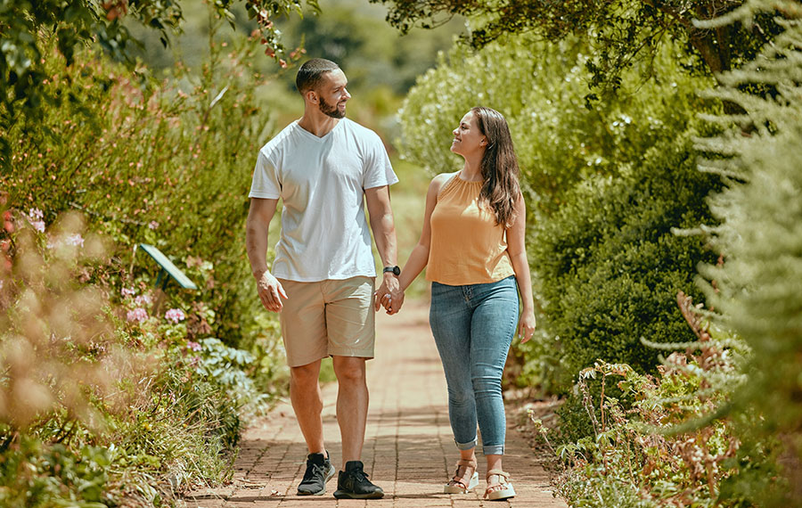 couple hand holding and walking along sunny garden path
